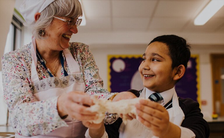 Member of teaching staff enjoying cookery lesson with junior school pupil