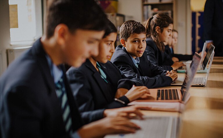 A group of children working on laptops in a classroom
