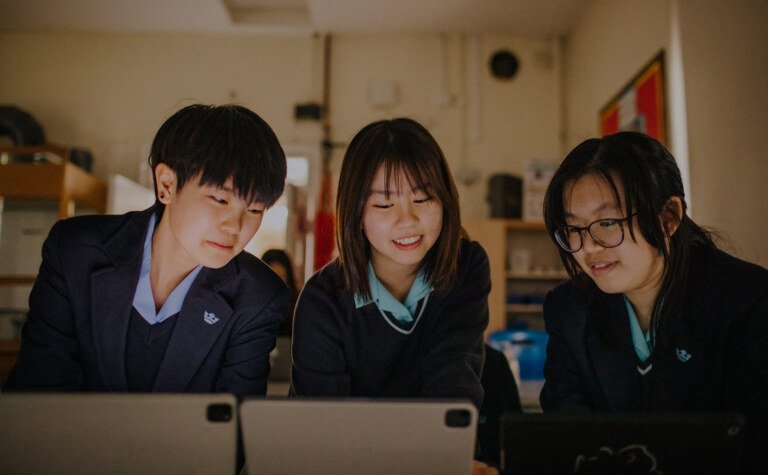 Three girls in a classroom looking at laptop screens