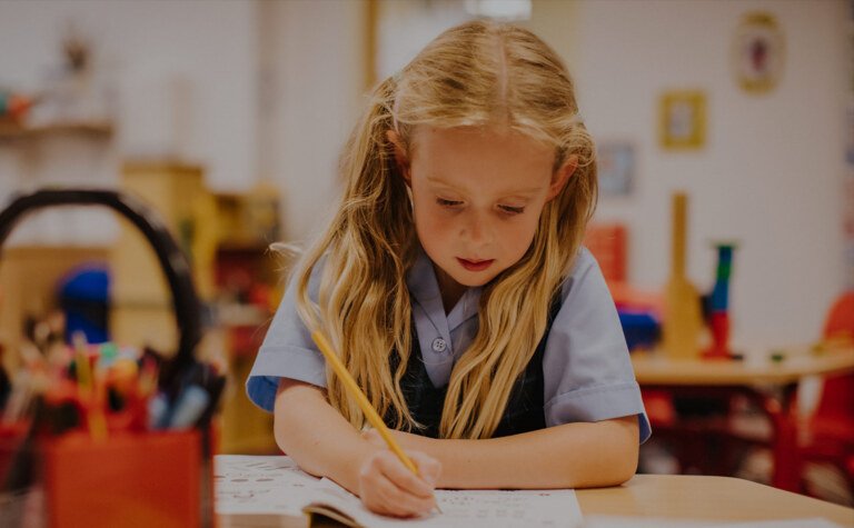 A little girl sitting at a desk  in school writing in a book