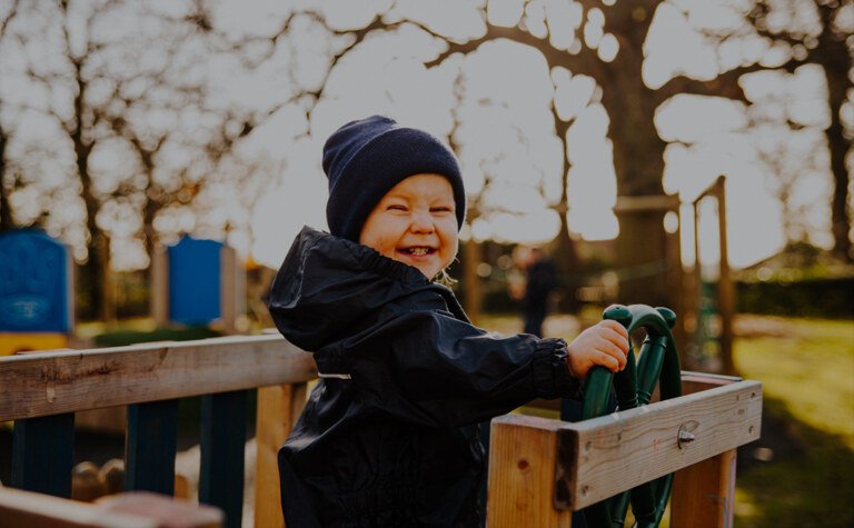 A nursery child playing outside on a wooden pirate ship