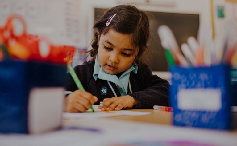 Reception age pupil concentrating hard on writing in classroom at St Margaret's School