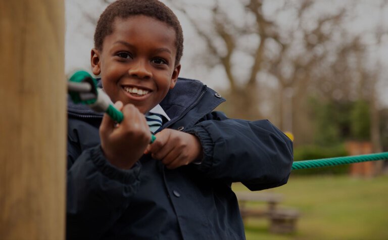 Happy upper junior school boy smiling and playing on climbing frame outside St Margaret's School