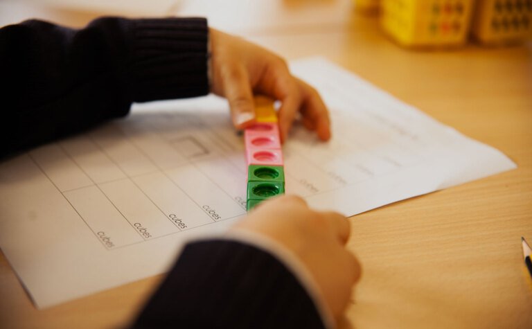 Close up of lower junior school pupil's hands with mathematical cubes learning in classroom