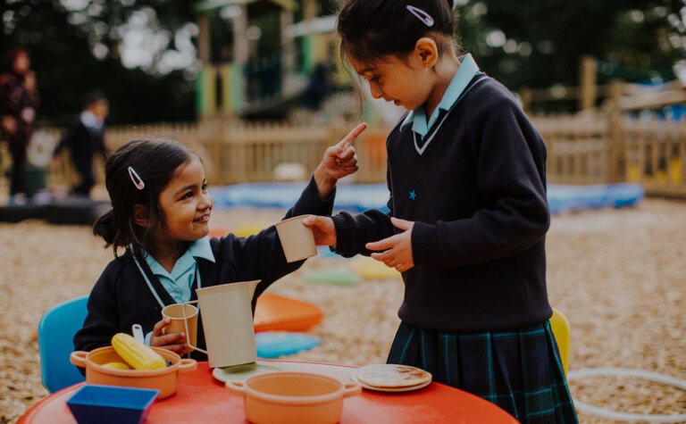 Two lower junior pupils holding a pretend tea party outside during after school care at St Margaret's School Bushey