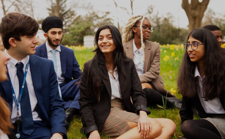 Group of sixth form students sat together on grass outside at St Margaret's School Bushey