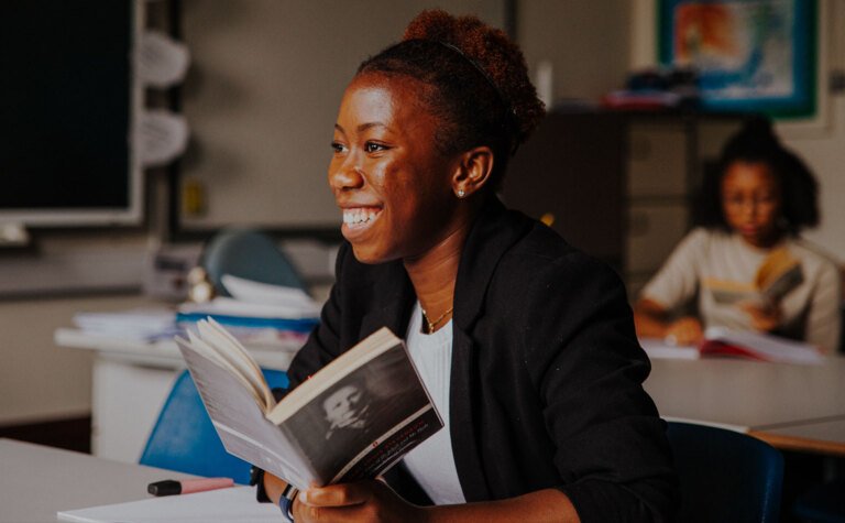 Smiling sixth form girl reading book in classroom at St Margaret's School Bushey