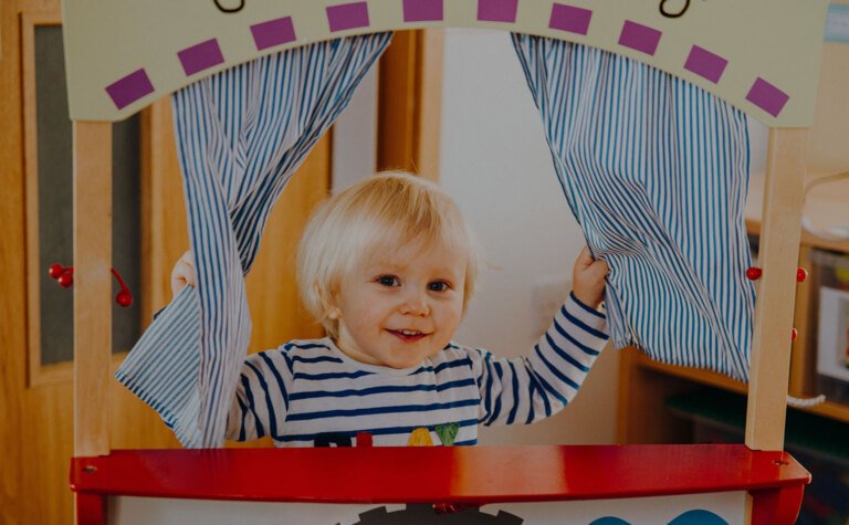 Nursery age child playing peek-a-boo in play area at St Margaret's School Bushey Nursery