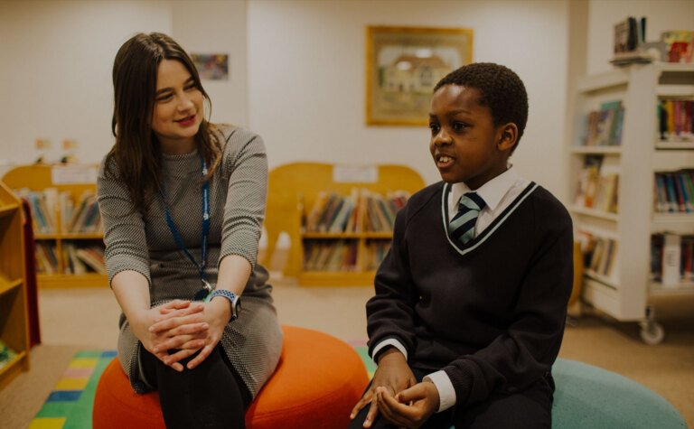 Upper junior school pupil sitting in library talking with a teacher at St Margaret's School