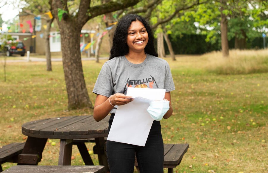 St Margarets School A level Student opening exam results envelope in orchard on results day 2020