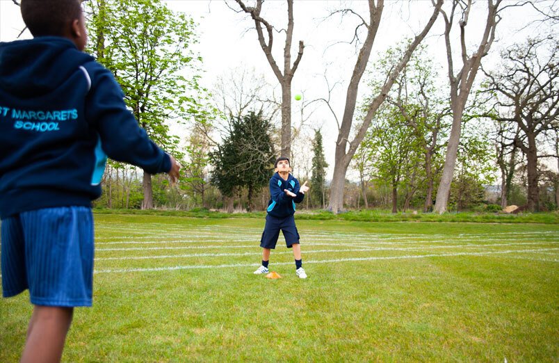 Young male Junior School pupil at St Margarets School catching a tennis ball thrown by classmate during cricket practice at school