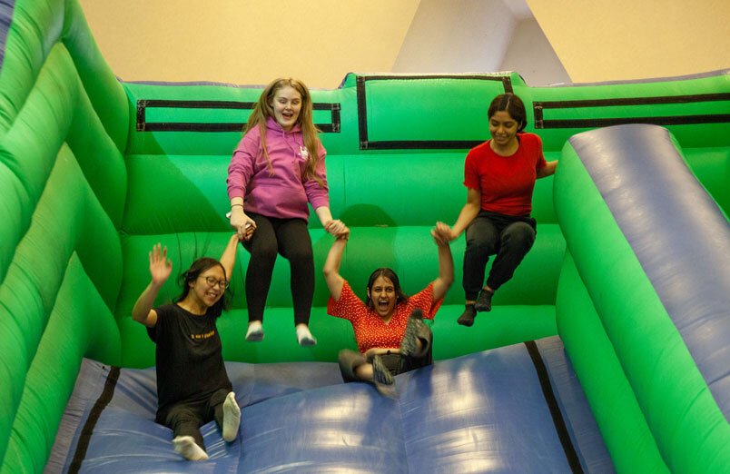 Four of St Margaret's Sixth Form Students bouncing on bouncy castle slide at party