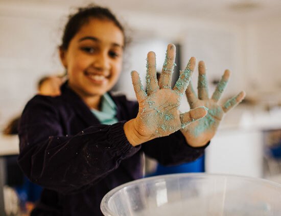 Junior School pupil smiling and showing sand covered hands whilst learning at St Margaret's School