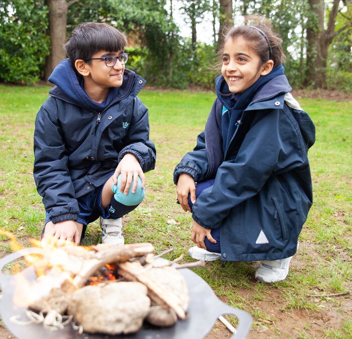 Two pupils from St Margaret's Junior School sat round a camp fire in an Outdoor Education lesson