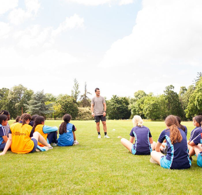 Group of St Margaret's Senior School pupils sitting on playing field during sports masterclass