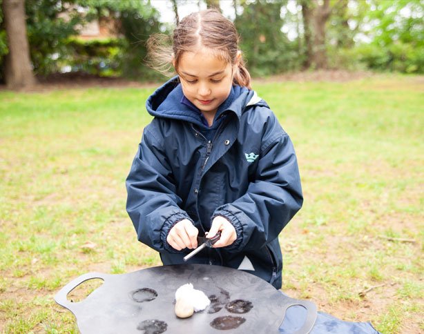 Young girl from St Margaret's Junior School trying to create a spark to light the fire pit